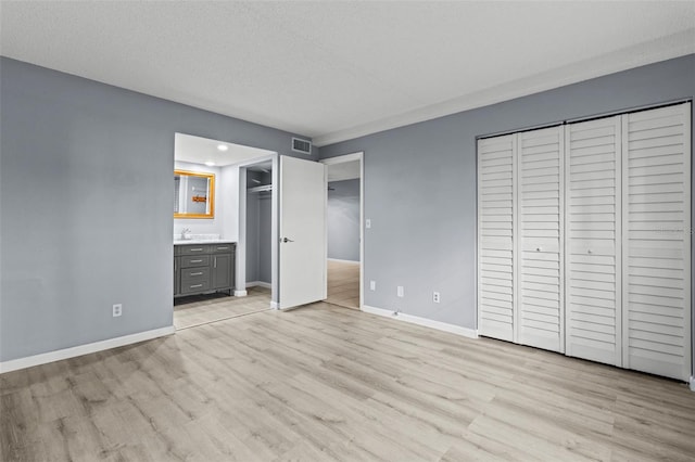 unfurnished bedroom featuring ensuite bathroom, light hardwood / wood-style floors, sink, and a textured ceiling