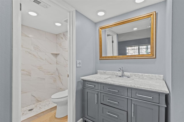 bathroom featuring hardwood / wood-style flooring, vanity, toilet, and a tile shower