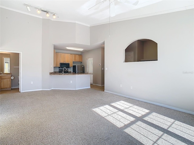 unfurnished living room with sink, ornamental molding, light carpet, and a high ceiling