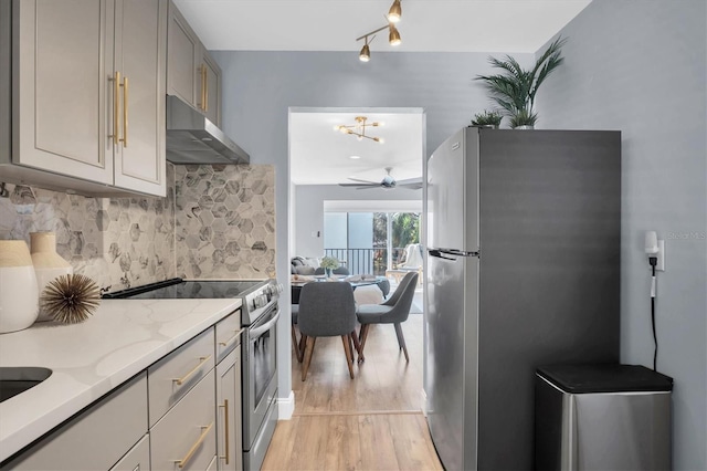 kitchen with gray cabinets, light stone countertops, appliances with stainless steel finishes, tasteful backsplash, and light hardwood / wood-style floors