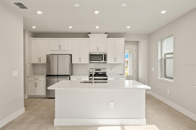 kitchen featuring a kitchen island with sink, decorative backsplash, white cabinets, and appliances with stainless steel finishes