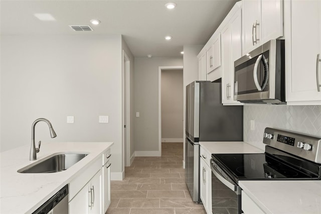 kitchen featuring sink, white cabinetry, appliances with stainless steel finishes, light stone countertops, and backsplash