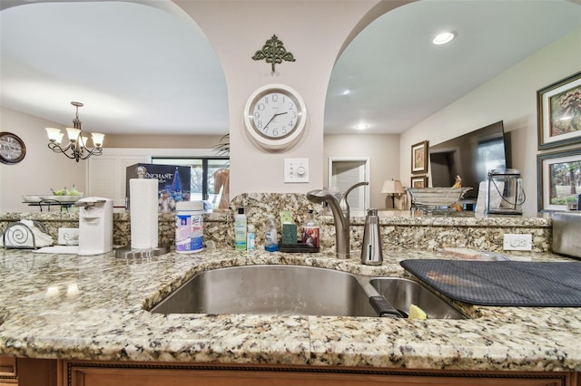 kitchen with pendant lighting, a notable chandelier, light stone countertops, and sink