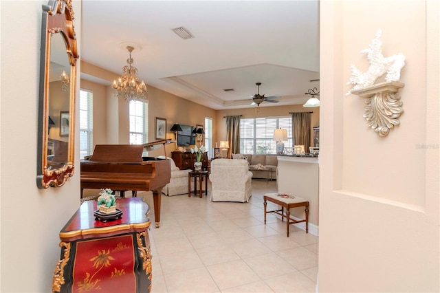 tiled living room featuring a raised ceiling and ceiling fan with notable chandelier