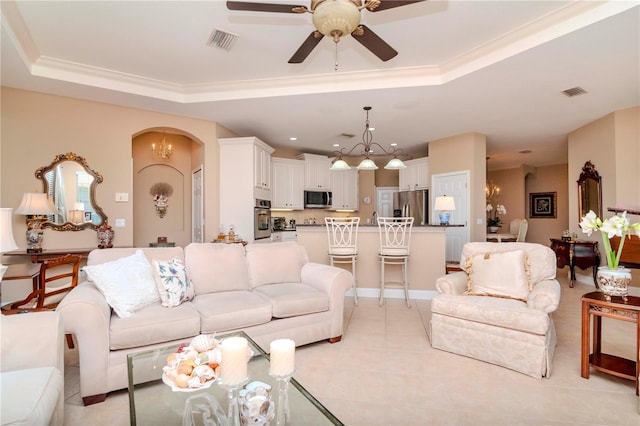 living room featuring ceiling fan with notable chandelier, light tile patterned floors, ornamental molding, and a tray ceiling