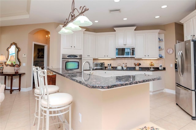 kitchen with tasteful backsplash, dark stone counters, stainless steel appliances, pendant lighting, and white cabinets