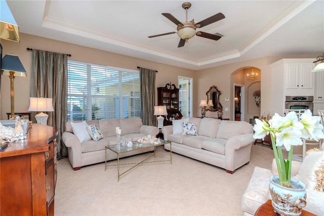 tiled living room featuring ceiling fan with notable chandelier and a tray ceiling