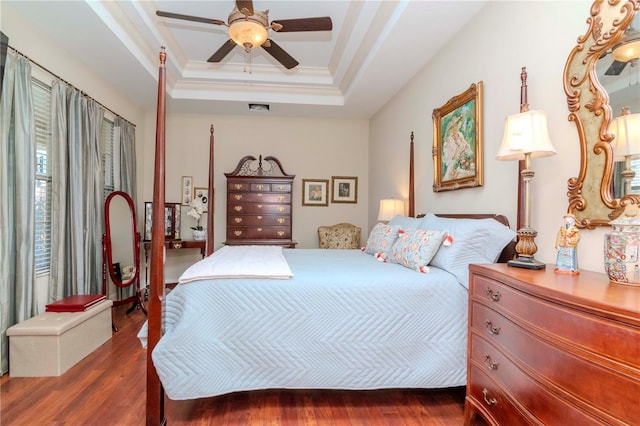 bedroom with dark hardwood / wood-style floors, ceiling fan, crown molding, and a tray ceiling