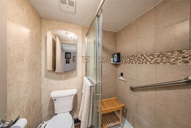 bathroom with toilet, a shower with shower door, and tile walls