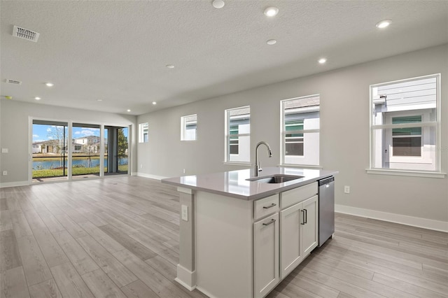 kitchen with sink, light hardwood / wood-style floors, an island with sink, white cabinets, and stainless steel dishwasher