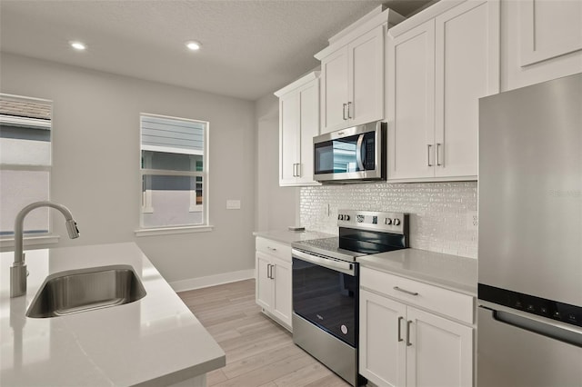 kitchen with white cabinetry, appliances with stainless steel finishes, sink, and light hardwood / wood-style flooring