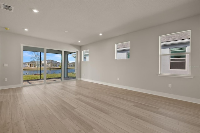 unfurnished room featuring a water view, a textured ceiling, and light hardwood / wood-style floors