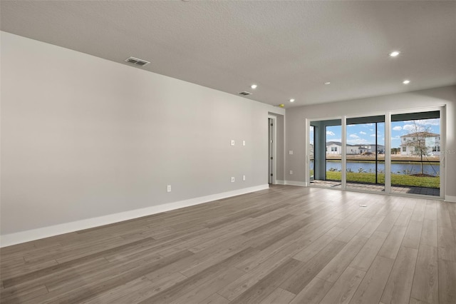 empty room with a water view, light hardwood / wood-style floors, and a textured ceiling