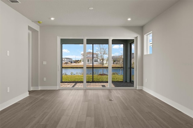 empty room with a water view, a healthy amount of sunlight, and wood-type flooring