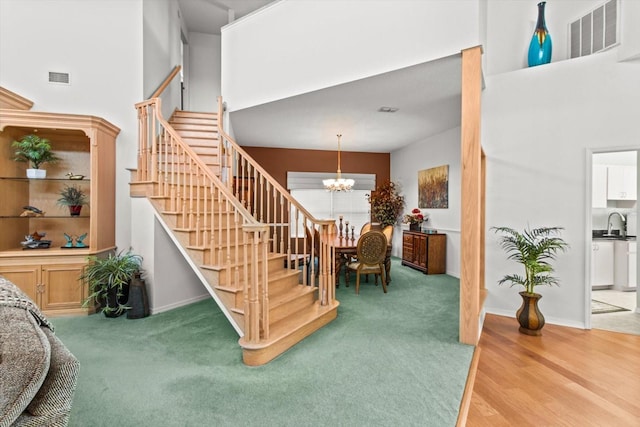 staircase featuring hardwood / wood-style flooring, sink, a towering ceiling, and an inviting chandelier