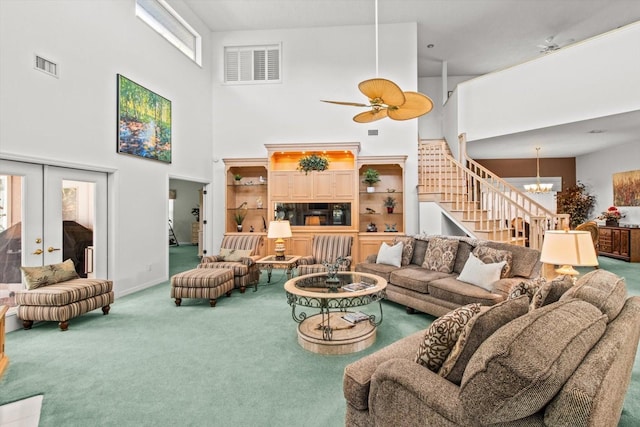 carpeted living room featuring ceiling fan with notable chandelier, a high ceiling, and french doors