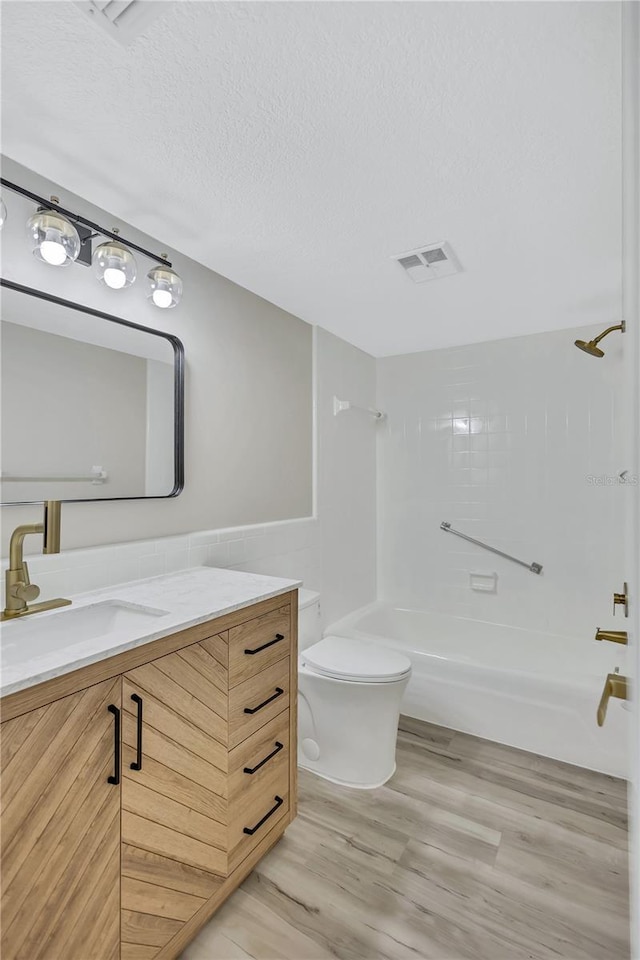 full bathroom featuring hardwood / wood-style floors, vanity, tiled shower / bath, toilet, and a textured ceiling