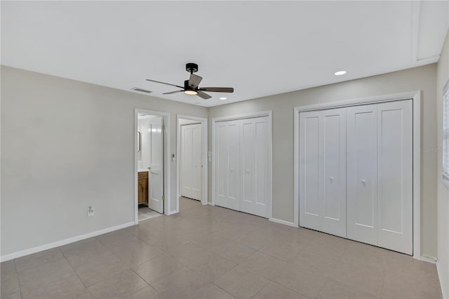 unfurnished bedroom featuring connected bathroom, ceiling fan, light tile patterned floors, and multiple closets