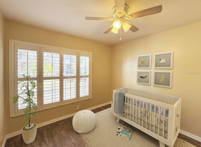 bedroom with ceiling fan, dark hardwood / wood-style flooring, and a nursery area