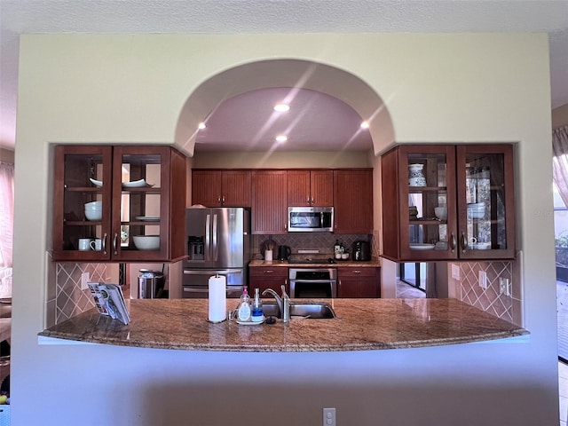 kitchen featuring sink, decorative backsplash, dark stone countertops, kitchen peninsula, and stainless steel appliances