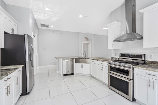 kitchen featuring wall chimney exhaust hood, stone countertops, decorative backsplash, white cabinets, and appliances with stainless steel finishes