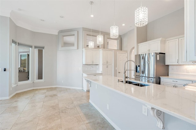 kitchen with pendant lighting, stainless steel fridge, light stone countertops, and white cabinetry