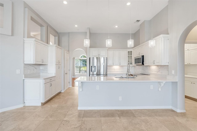 kitchen with white cabinets, a towering ceiling, stainless steel appliances, and hanging light fixtures