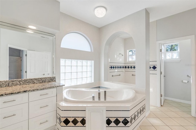 bathroom with tile patterned flooring, vanity, tiled bath, and a healthy amount of sunlight