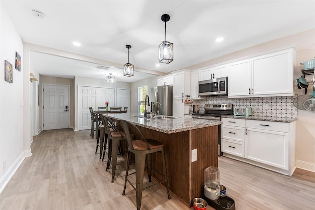 kitchen with white cabinets, stainless steel appliances, an island with sink, sink, and light stone counters