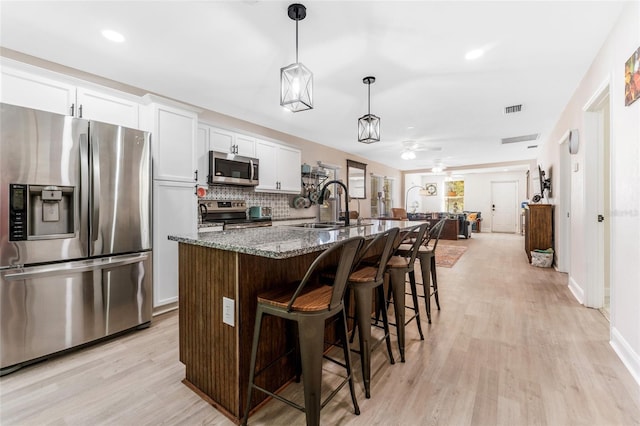 kitchen with appliances with stainless steel finishes, white cabinetry, sink, dark stone countertops, and a center island with sink