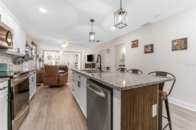 kitchen with white cabinetry, a sink, appliances with stainless steel finishes, a kitchen bar, and light wood finished floors