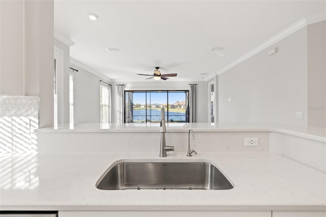 kitchen featuring light stone counters, sink, ceiling fan, and ornamental molding