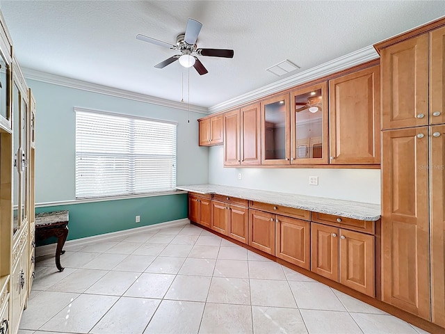 kitchen featuring ceiling fan, light stone countertops, ornamental molding, and light tile patterned floors