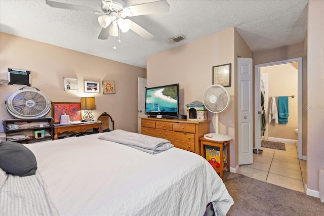 bedroom featuring ceiling fan, light tile patterned floors, ensuite bathroom, and a textured ceiling