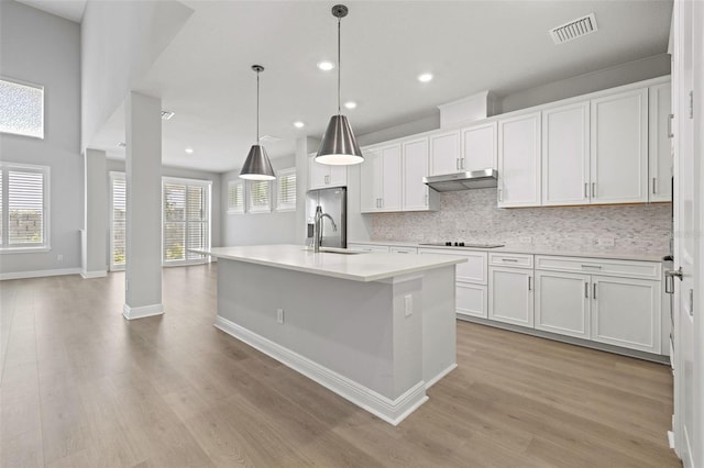 kitchen with a kitchen island with sink, light hardwood / wood-style flooring, white cabinets, and decorative light fixtures