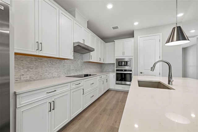 kitchen with appliances with stainless steel finishes, hanging light fixtures, under cabinet range hood, white cabinetry, and a sink