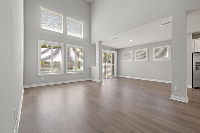 unfurnished living room featuring visible vents, plenty of natural light, baseboards, and wood finished floors