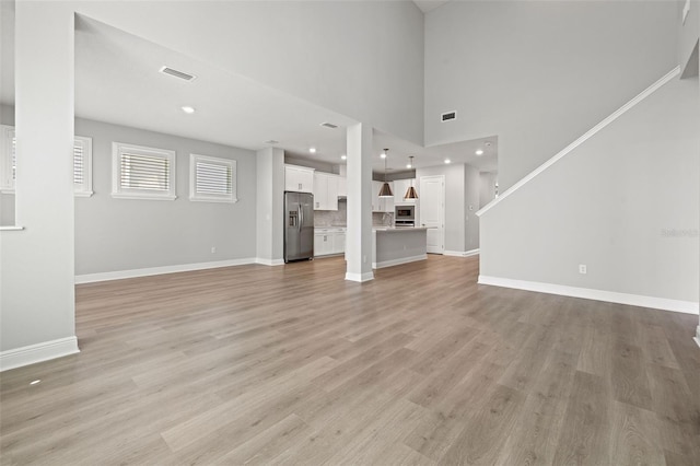 unfurnished living room featuring light wood finished floors, visible vents, baseboards, and recessed lighting