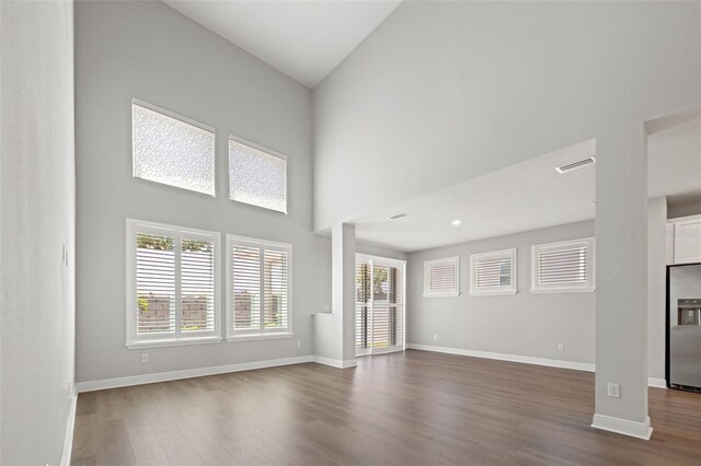 unfurnished living room with a towering ceiling, visible vents, baseboards, and dark wood-type flooring