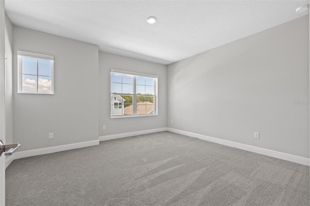 carpeted empty room featuring a textured ceiling and baseboards