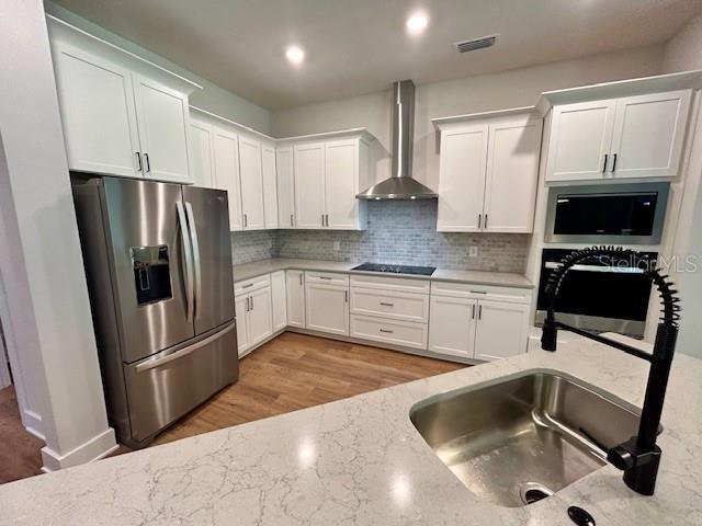 13400 Haflinger Way, Hudson, FL 34667 - kitchen with appliances with stainless steel finishes, wall chimney range hood, light wood-type flooring, and white cabinets