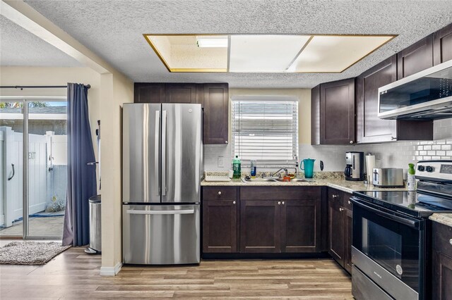 kitchen with sink, light wood-type flooring, a textured ceiling, appliances with stainless steel finishes, and tasteful backsplash