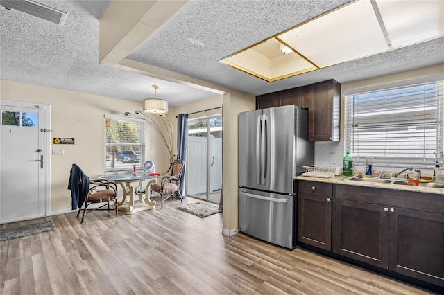 kitchen with stainless steel refrigerator, dark brown cabinetry, sink, light hardwood / wood-style flooring, and a textured ceiling