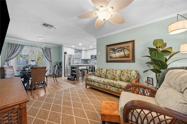 living room with a textured ceiling, ceiling fan, light hardwood / wood-style floors, and crown molding