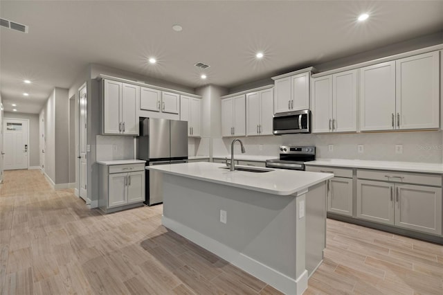 kitchen with appliances with stainless steel finishes, sink, a kitchen island with sink, and light hardwood / wood-style floors