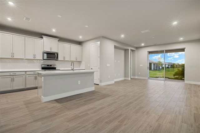 kitchen featuring white cabinetry, decorative backsplash, stainless steel appliances, a center island with sink, and light hardwood / wood-style flooring