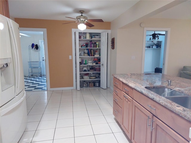 kitchen featuring white refrigerator with ice dispenser, sink, ceiling fan, light tile patterned flooring, and light stone counters