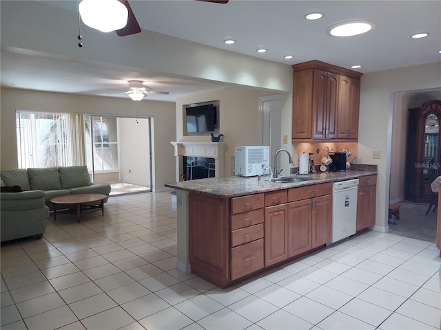 kitchen featuring dishwasher, sink, ceiling fan, dark stone countertops, and light tile patterned floors