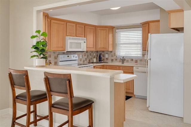 kitchen featuring kitchen peninsula, decorative backsplash, white appliances, light tile patterned floors, and a breakfast bar area