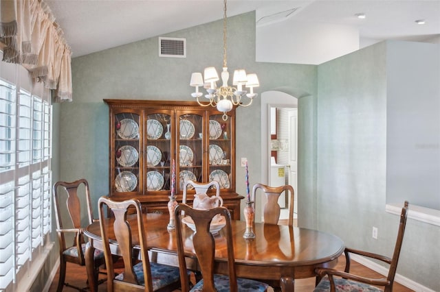 dining space featuring hardwood / wood-style floors, lofted ceiling, and an inviting chandelier